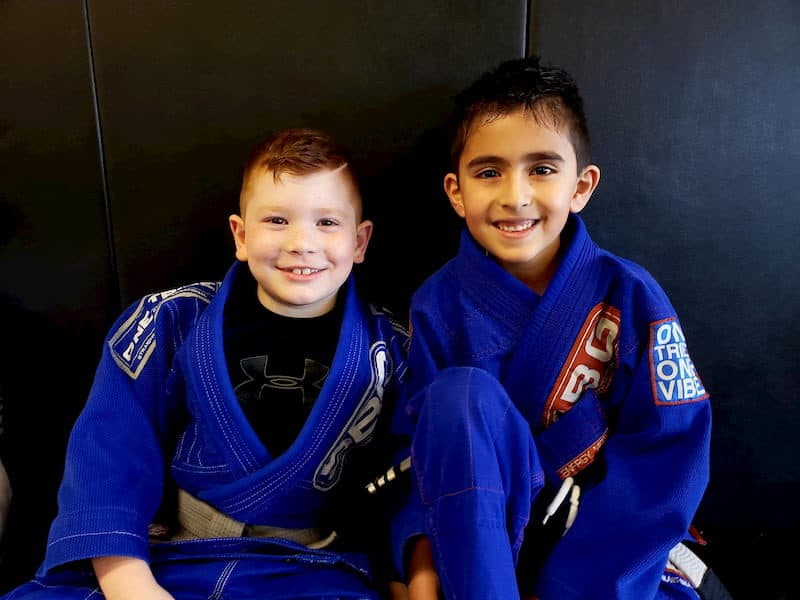 two kids Brazilian Jiu Jitsu students sitting side by side in blue gi